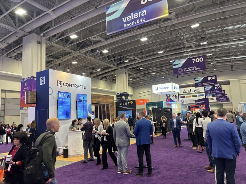 Busy GAC expo hall with attendees in business attire walking the purple carpet past vendor booths including Velera, N Contracts, and Zest AI under America's Credit Unions section signs